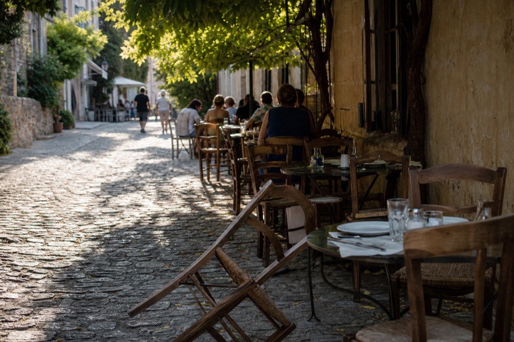 Bistro terrace with wooden chairs and small tables along a cobblestone lane, no text, no logos, no people