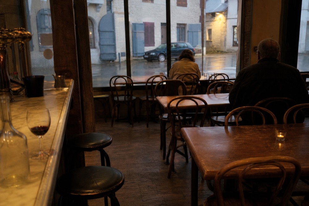 Interior of a small French bistro with wooden tables, bentwood chairs and a marble bar, no text, no logos, no people